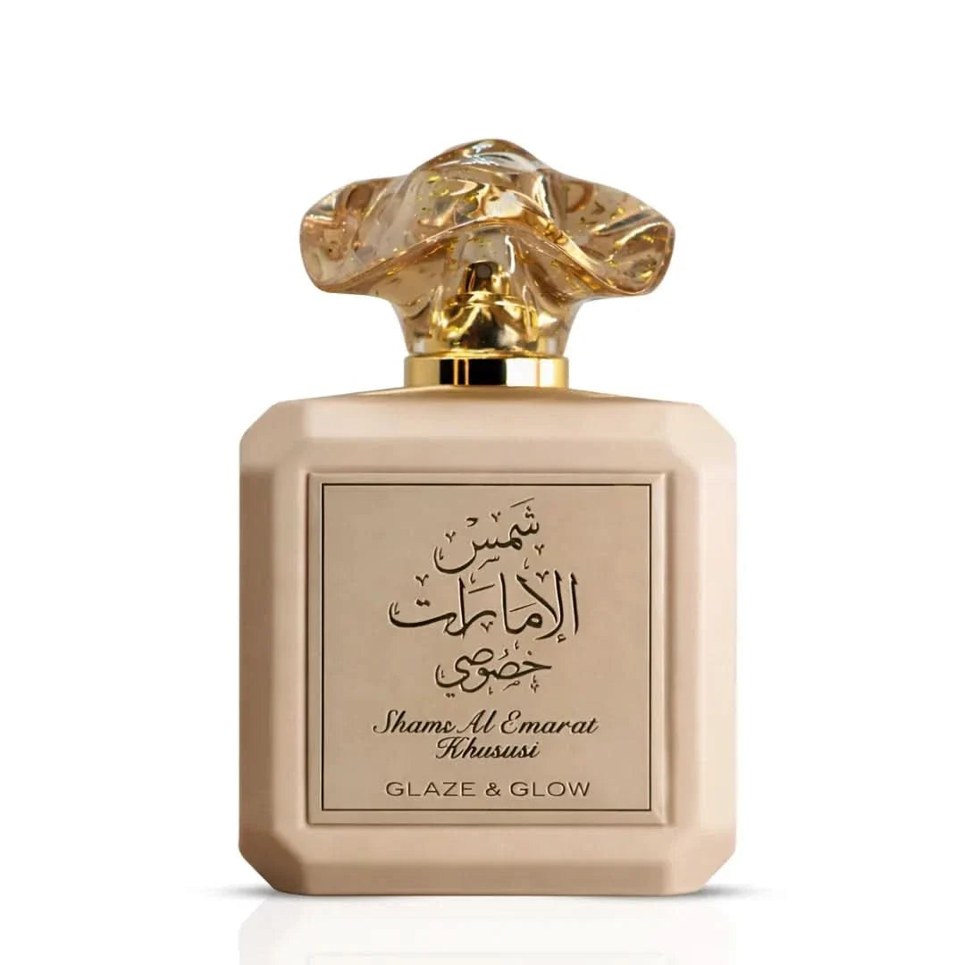 A beige rectangular perfume bottle with a sculptural gold cap, featuring Arabic calligraphy and the text 'Shame Al Emarat Khususi' and 'GLAZE & GLOW' on the front label.